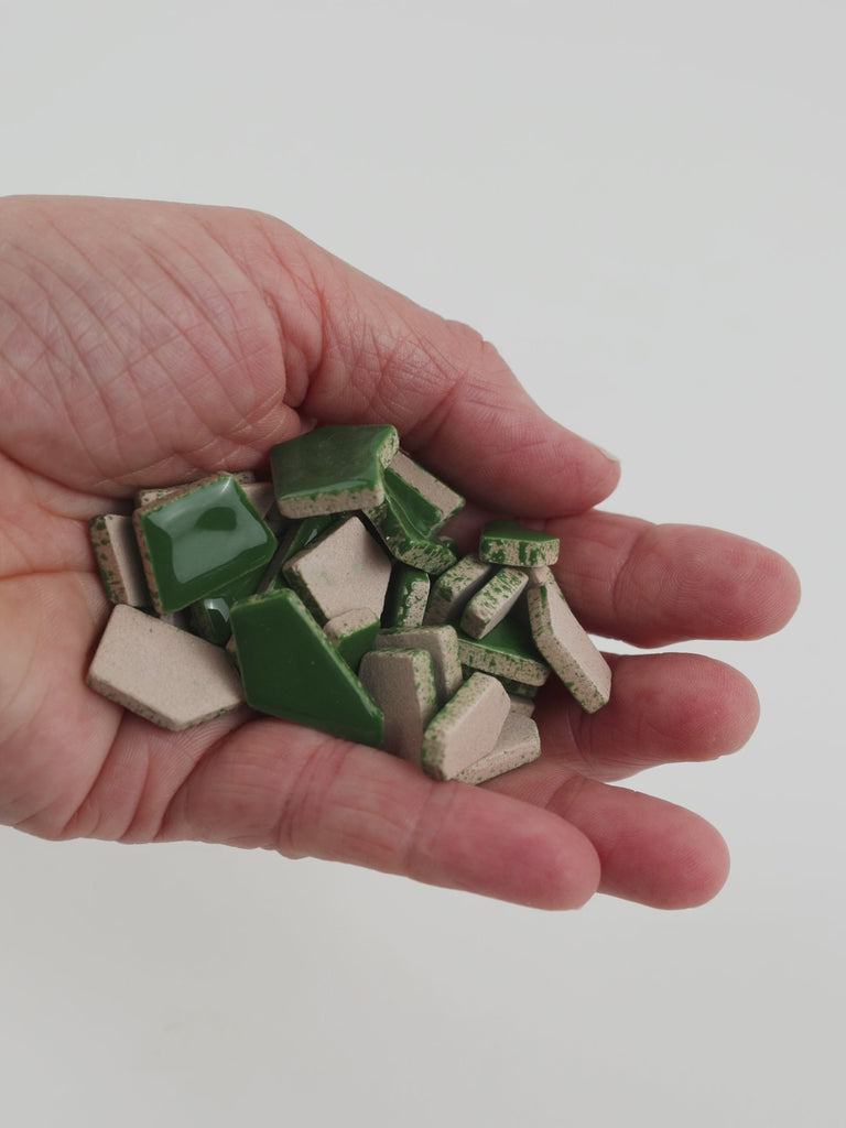 Video of Flip ceramic puzzle pieces in moss green, opaque glazed porcelain, 4–20 mm, held in a hand and poured out to show their shapes and finish