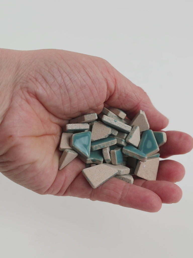 Video of Flip ceramic puzzle pieces in mint green, opaque glazed porcelain, 4–20 mm, held in a hand and poured out to show their shapes and finish