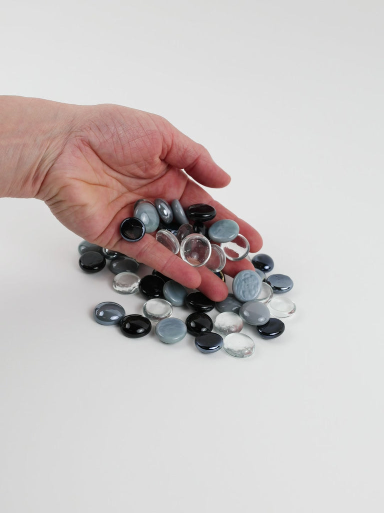 Video of white-black-grey mix glass nuggets in black, grey, white and clear shades with an iridescent sheen, 16–20 mm, picked up from a pile by hand and dropped back to show their size, round shape and shine