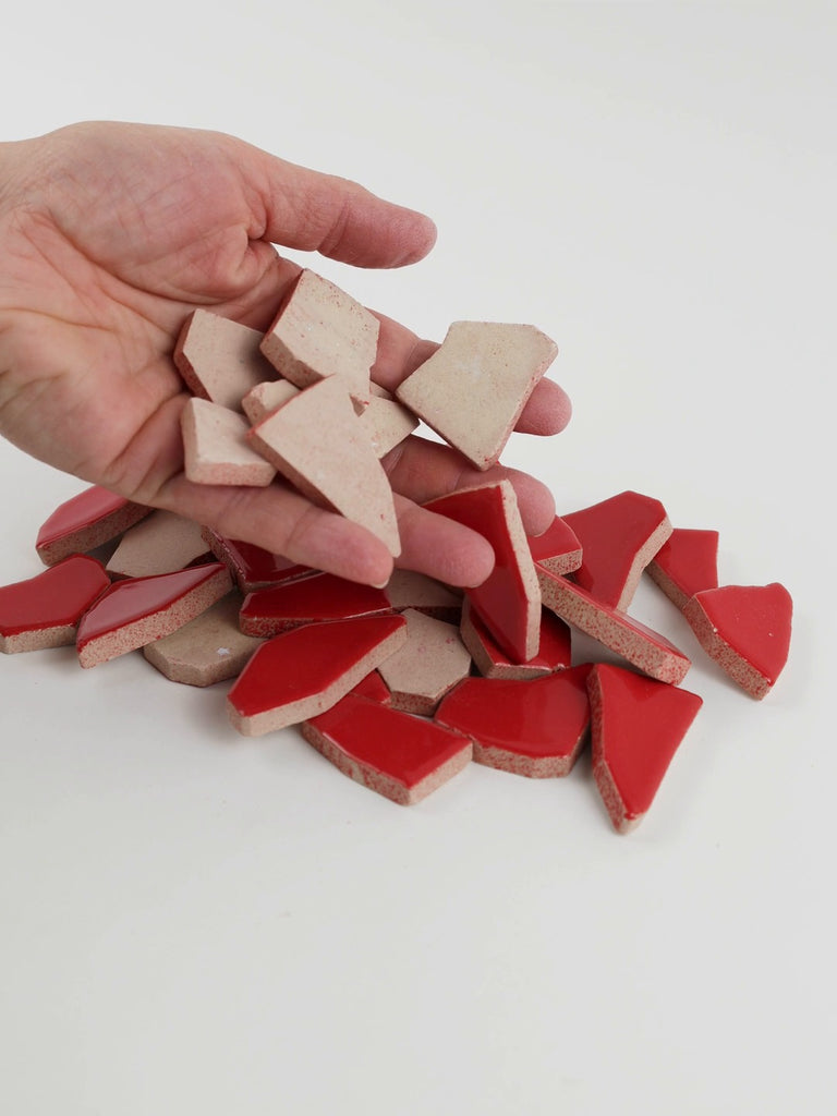 Video of Flip XL ceramic puzzle pieces in cherry red, opaque glazed porcelain, 20–60 mm, picked up from a pile by hand and dropped back to show their size, shapes and finish