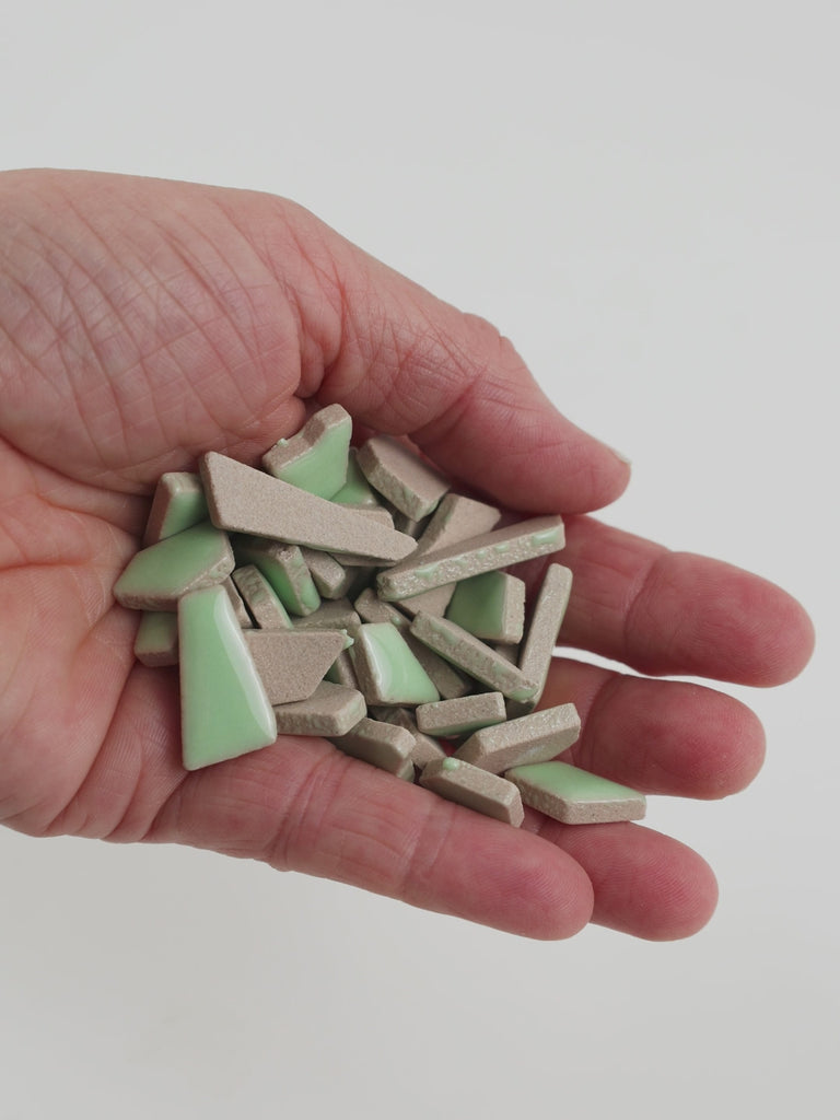 Video of Flip ceramic puzzle pieces in linden green, opaque glazed porcelain, 4–20 mm, held in a hand and poured out to show their shapes and finish